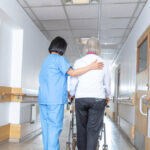 Asian doctor helping elder woman with walker in hospital hallway