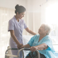 Asian young nurse supporting elderly patient disabled woman in using walker in hospital. Elderly patient care concept.