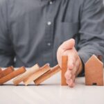 business man hand prevent falling wooden stick (dominoes) to the house model . risk management in business concept business man hand prevent falling wooden stick (dominoes) to the house model . risk management in business concept